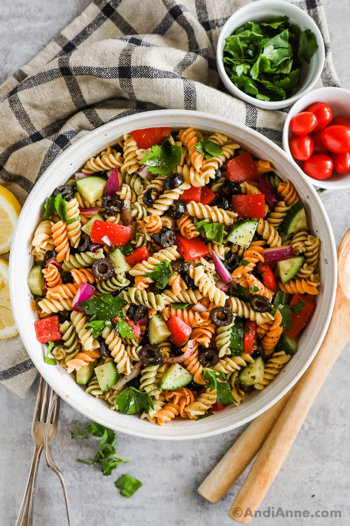 A bowl of italian pasta salad with rotini noodles, tomatoes, cucumbers, olives, parsley.