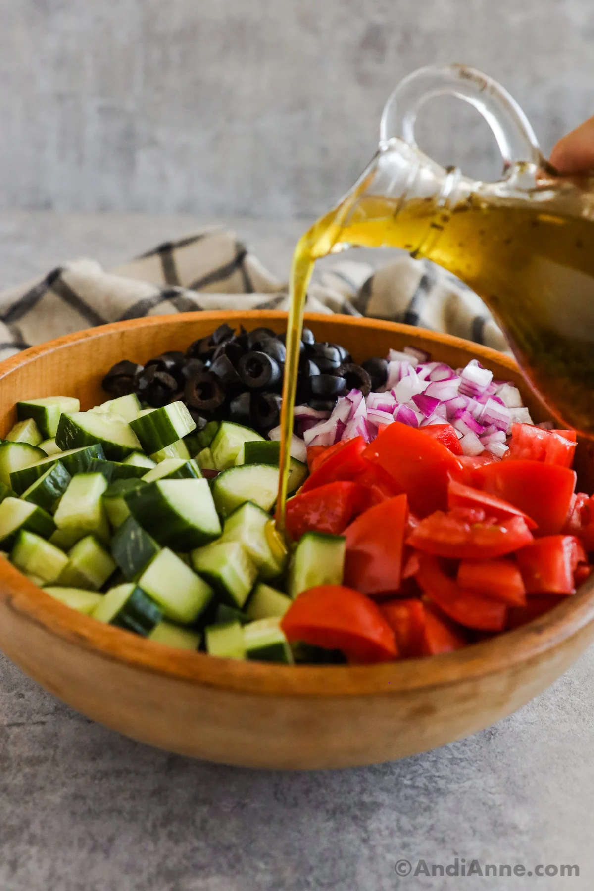 Salad dressing drizzled overtop of a salad with chopped cucumber, tomatoes, olives and onion.