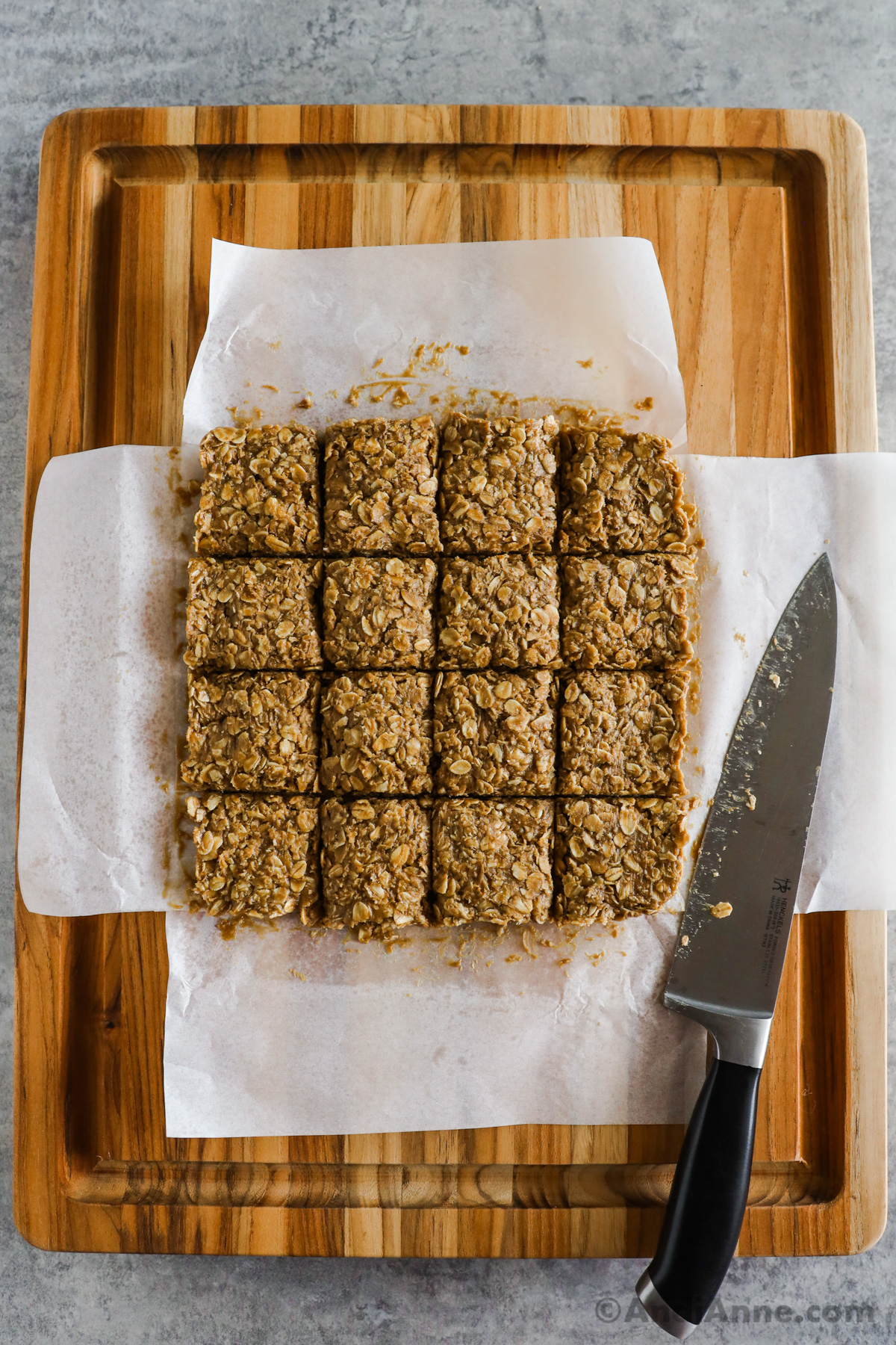 Sliced peanut butter oatmeal bars on parchment paper on a cutting board with a knife.