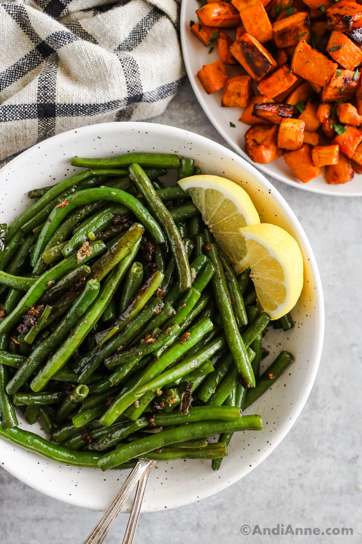 A plate of green beans with lemon wedges. A plate of baked chopped sweet potatoes beside.