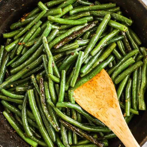 Cast iron skillet with sauteed green beans and a wood spatula.