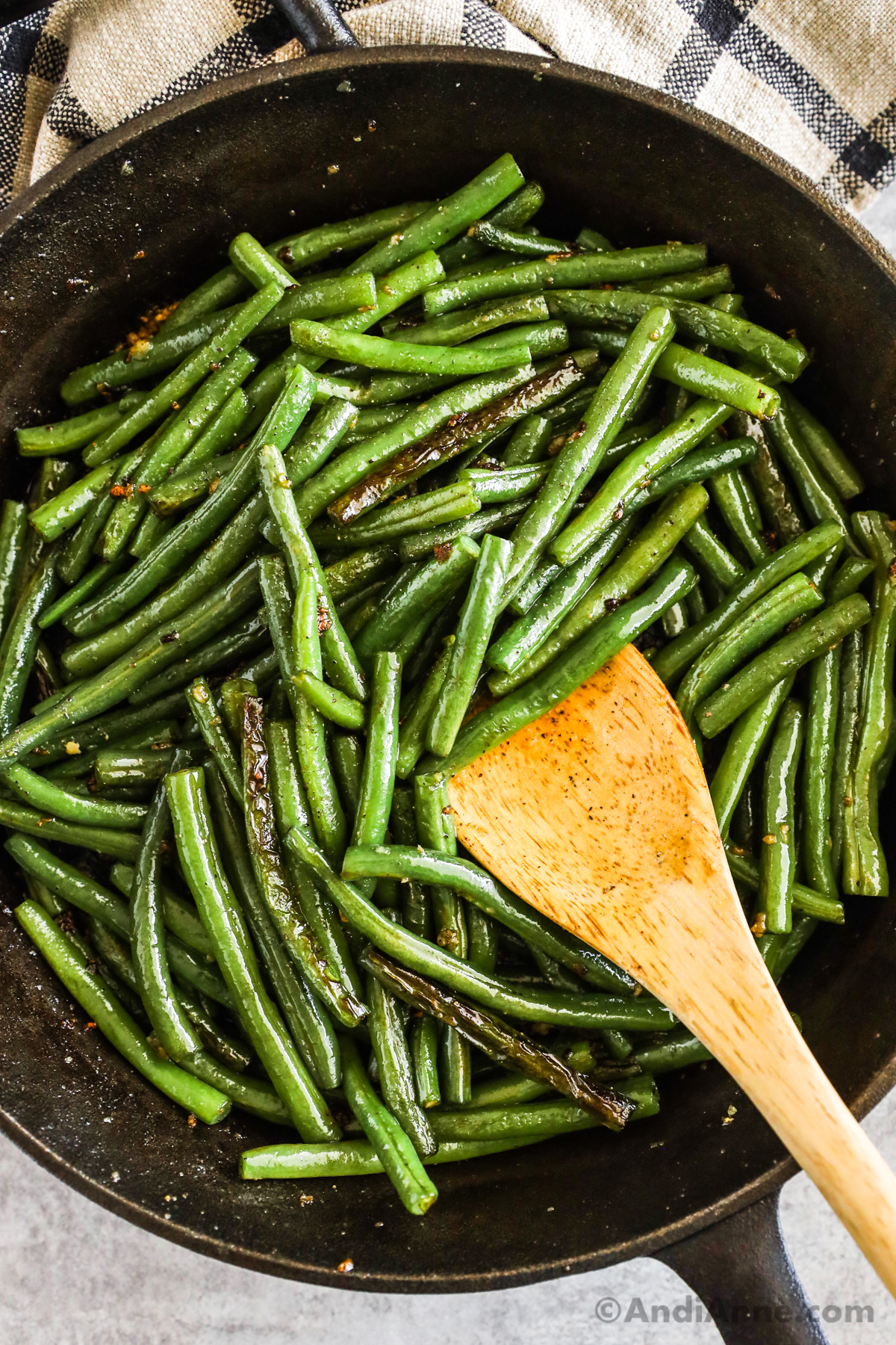 A frying pan with sauteed green beans and a wood spoon.