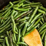 a frying pan with garlic butter sauteed green beans and a wood spoon