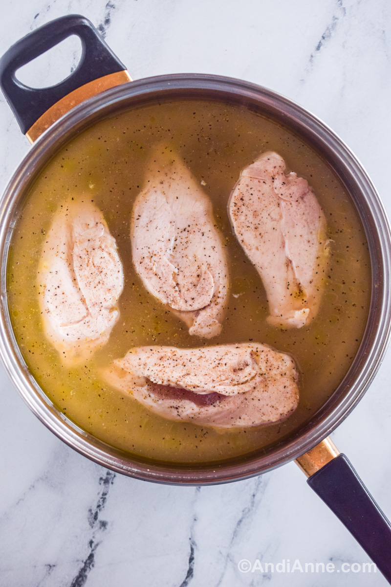 Four chicken breasts in broth liquid in a pot.