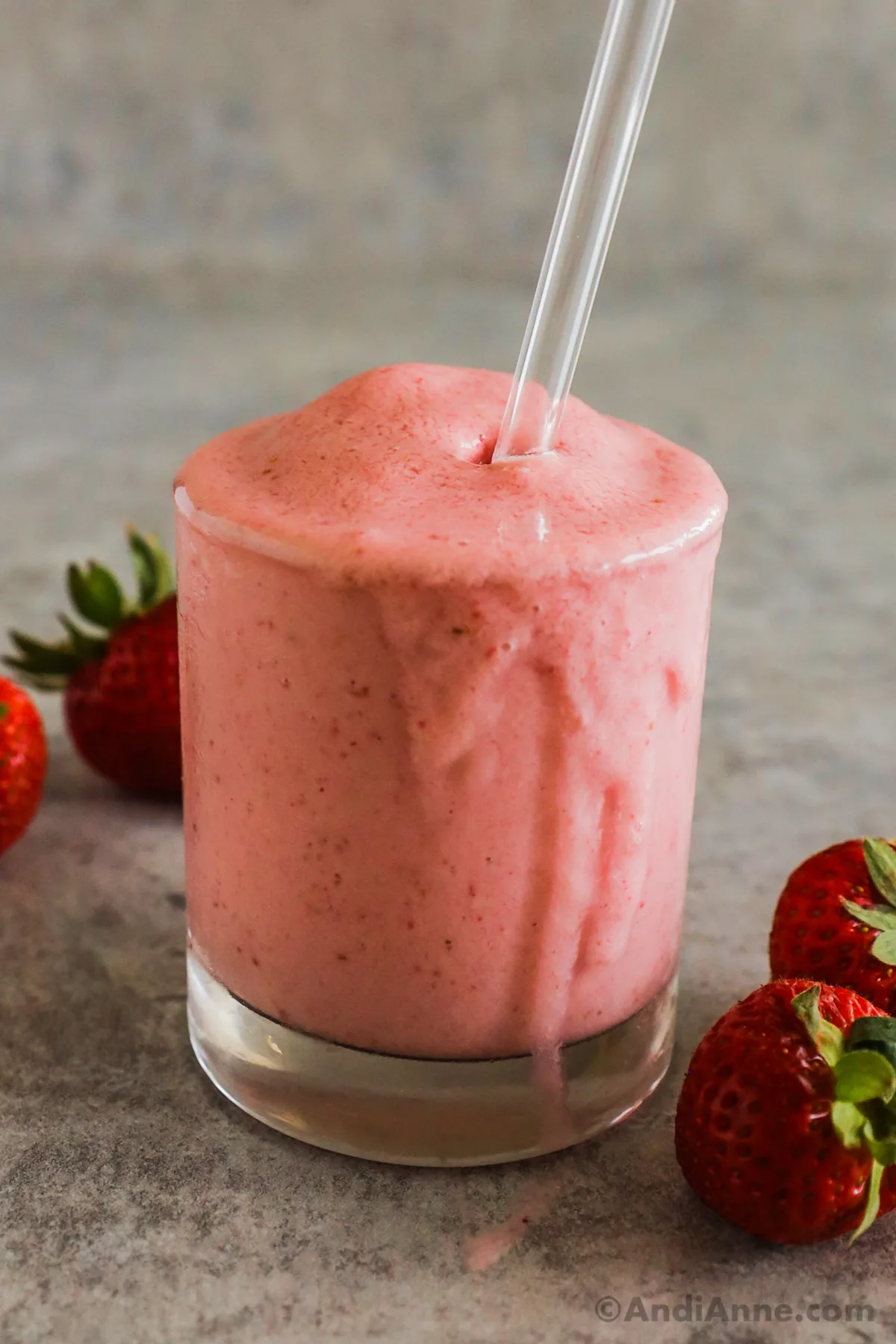 A strawberry banana smoothie with a straw and fresh strawberries around it.