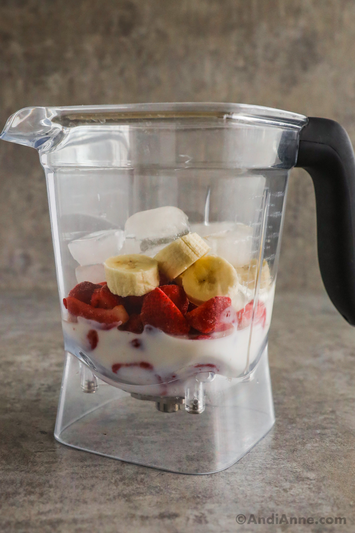 A blender with milk, sliced strawberries, sliced banana and ice cubes inside.