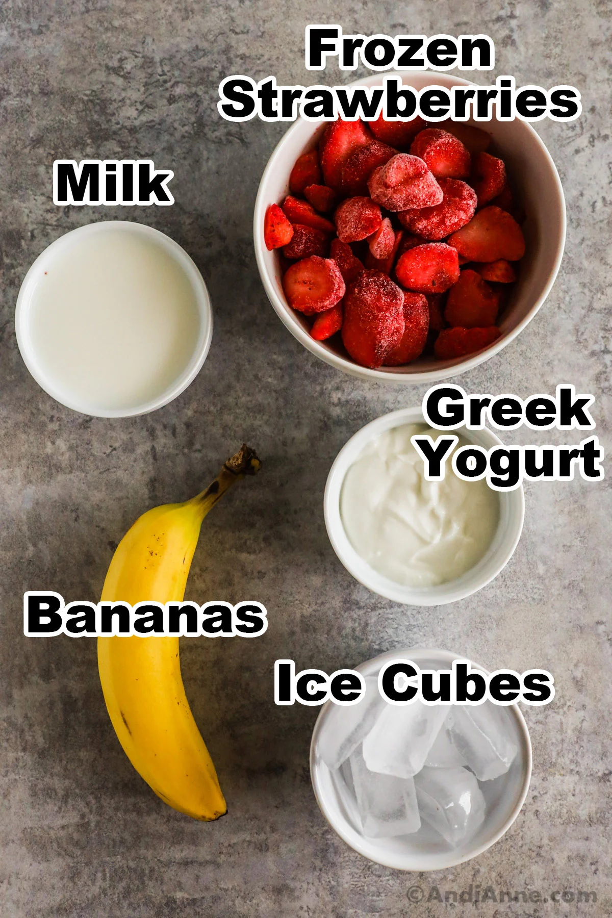 Bowls of frozen strawberries, milk, greek yogurt, a banana and ice cubes.