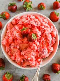 A bowl of strawberry jello fluff salad recipe surrounded by fresh strawberries.