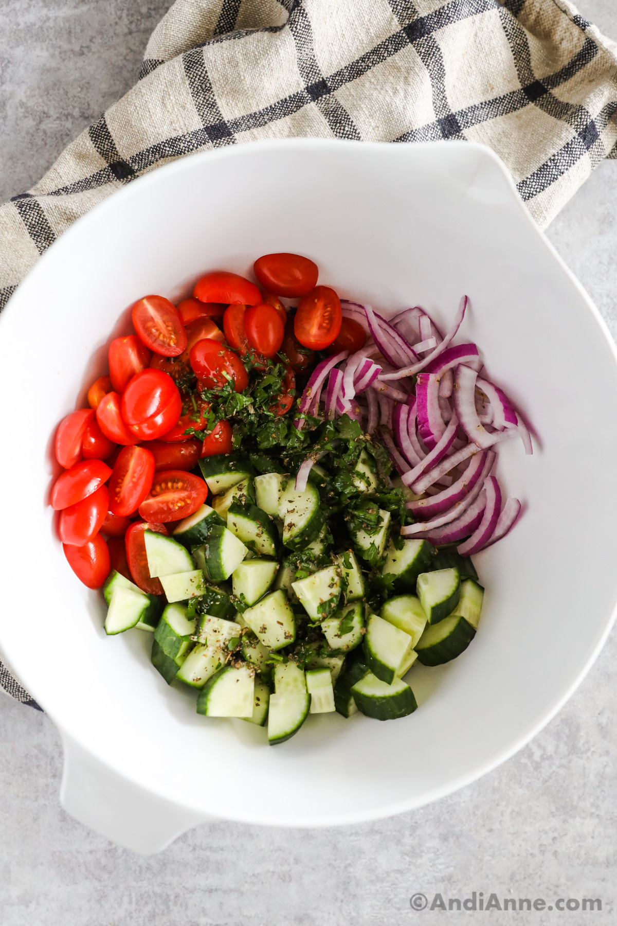 Grape tomatoes, sliced red onion and cucumber in a white bowl.