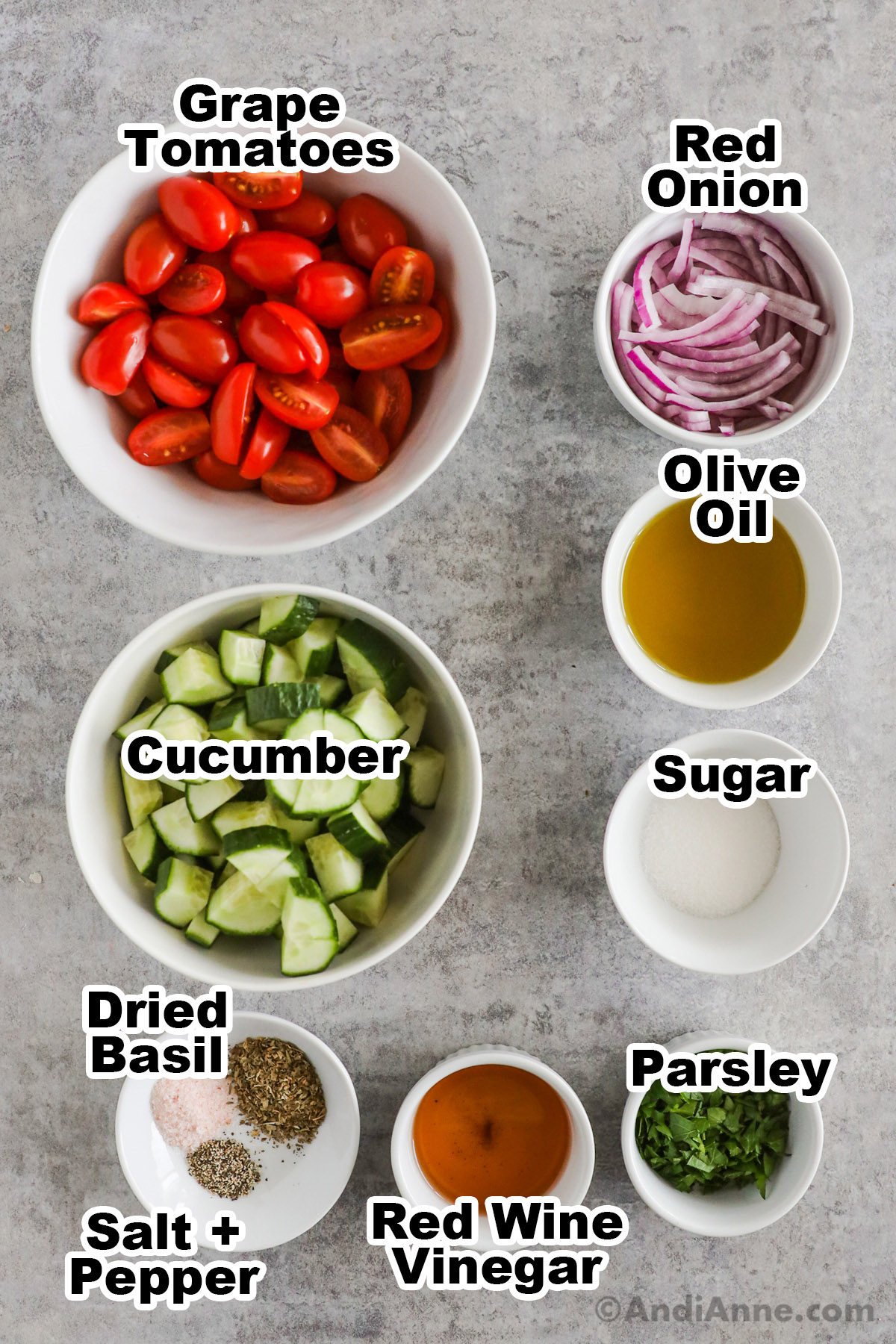 Recipe ingredients including bowls of grape tomatoes, sliced red onion, olive oil, cucumber, sugar, parsley, red wine vinegar, dried basil, salt and pepper.