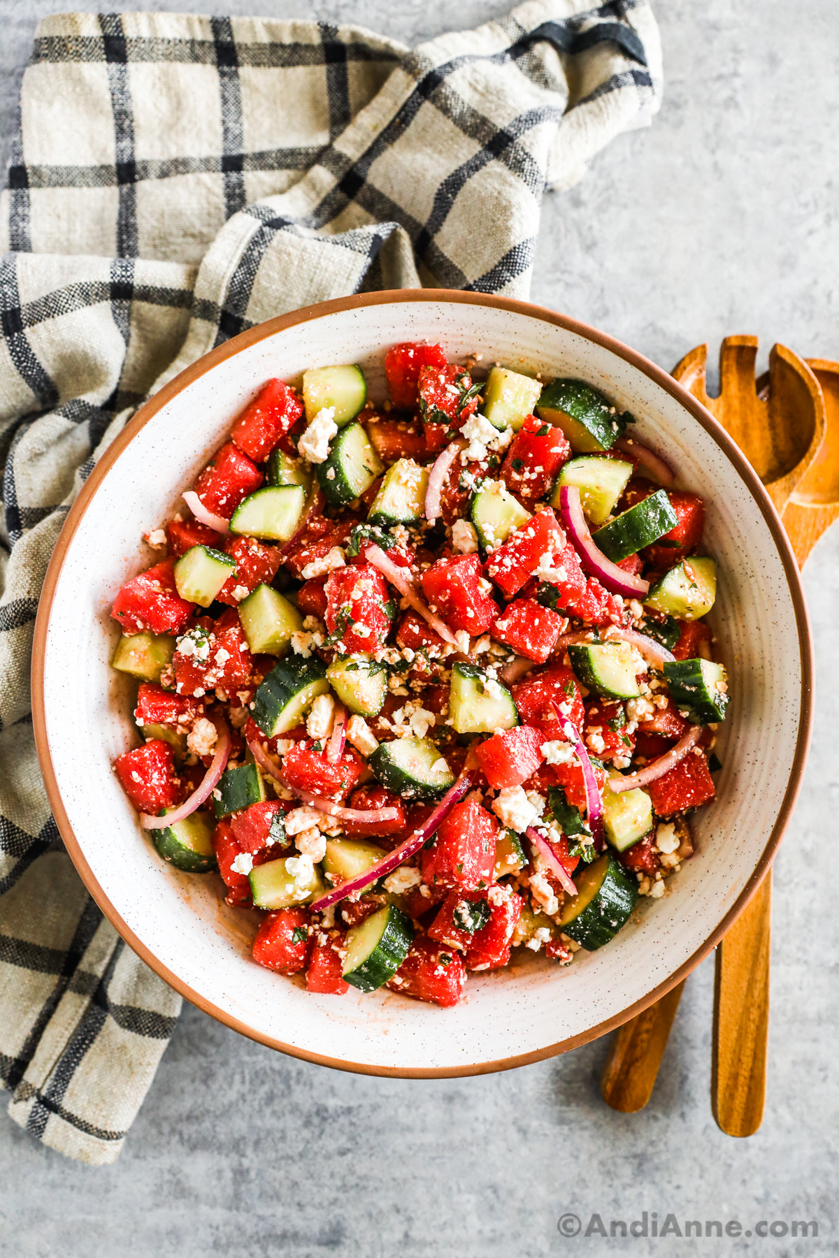 Watermelon cucumber salad in a large bowl with sliced onion and feta cheese.