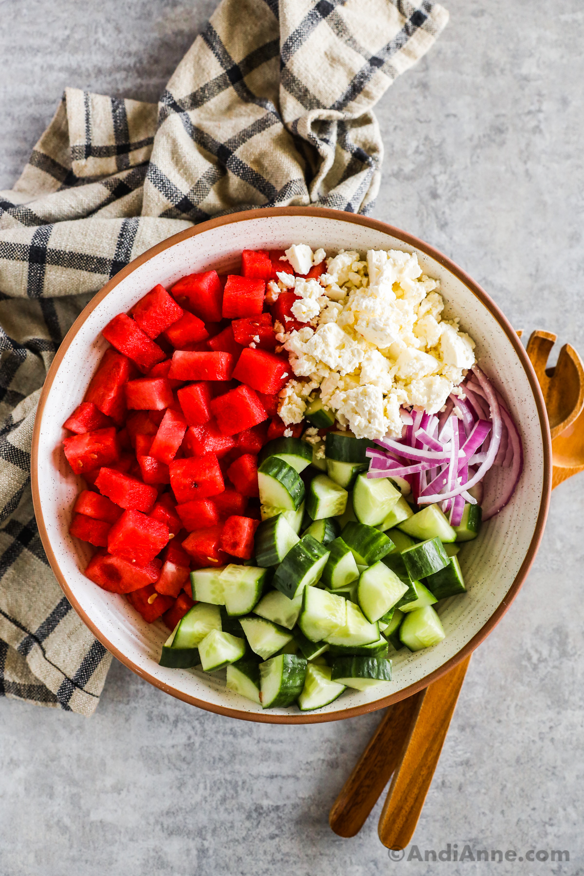 Chopped watermelon, feta cheese, cucumbers and sliced red onion in a large bowl.