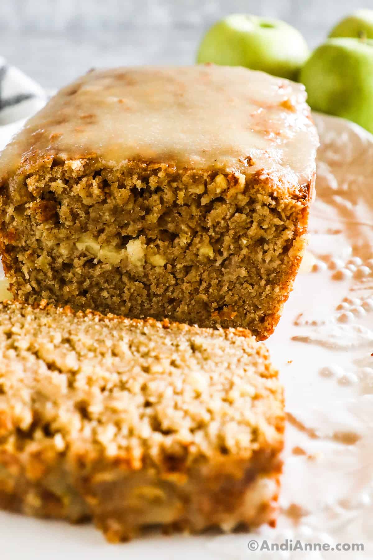 Closeupu of sliced open Apple Cinnamon Oatmeal Bread loaf with a slice lying in foreground. Granny Smith apples in background.
