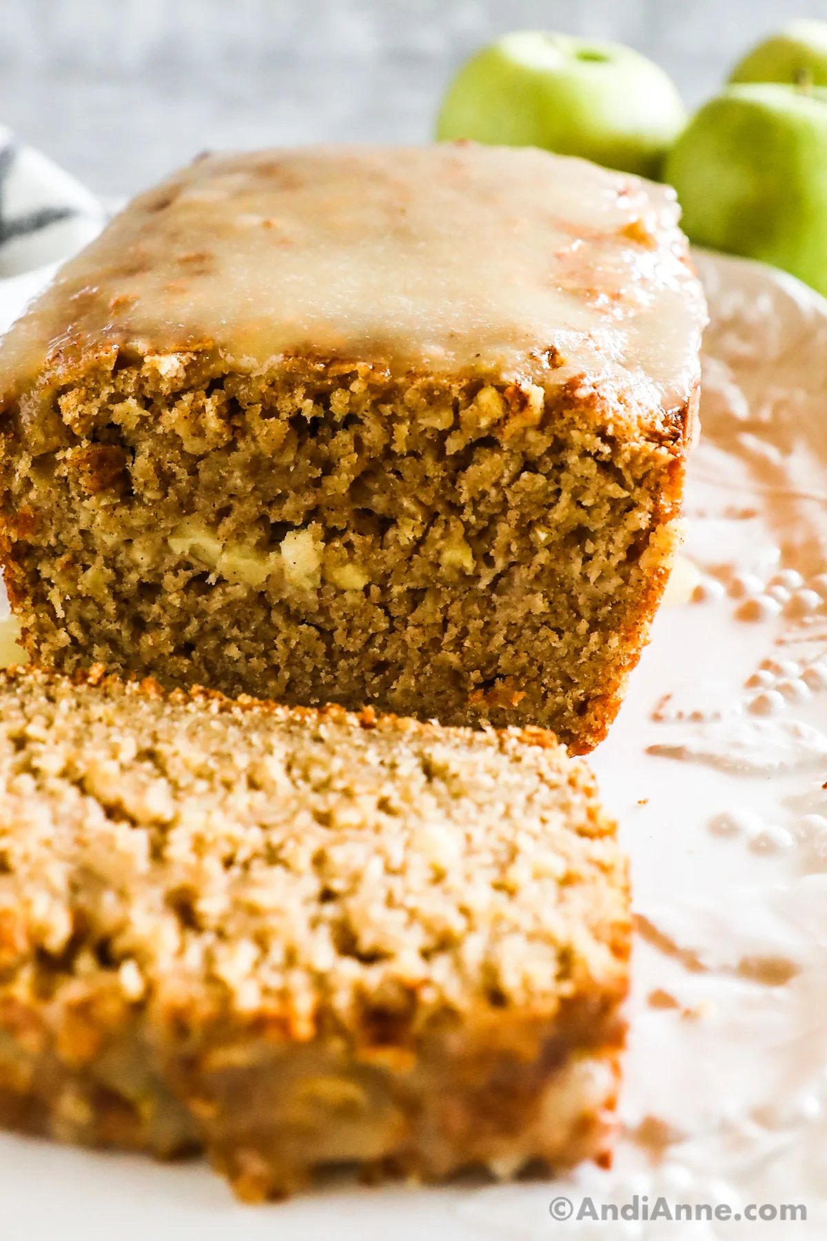 Closeupu of sliced open Apple Cinnamon Oatmeal Bread loaf with a slice lying in foreground. Granny Smith apples in background.
