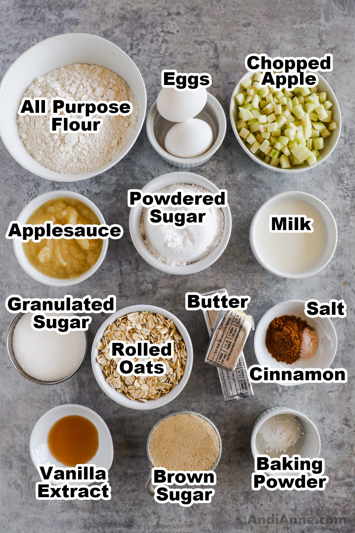 Overhead image of ingredients in separate bowls. All purpose flour, eggs, chopped apple, applesauce, powdered sugar, milk, granulated sugar, rolled oats, butter, salt, cinnamon, vanilla extract, brown sugar and baking powder.
