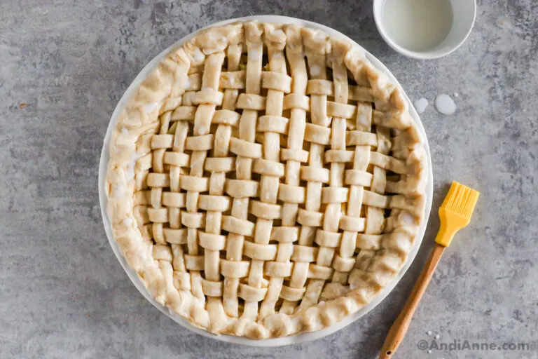 An unbaked pie with a lattice crust and a brush and bowl of milk.