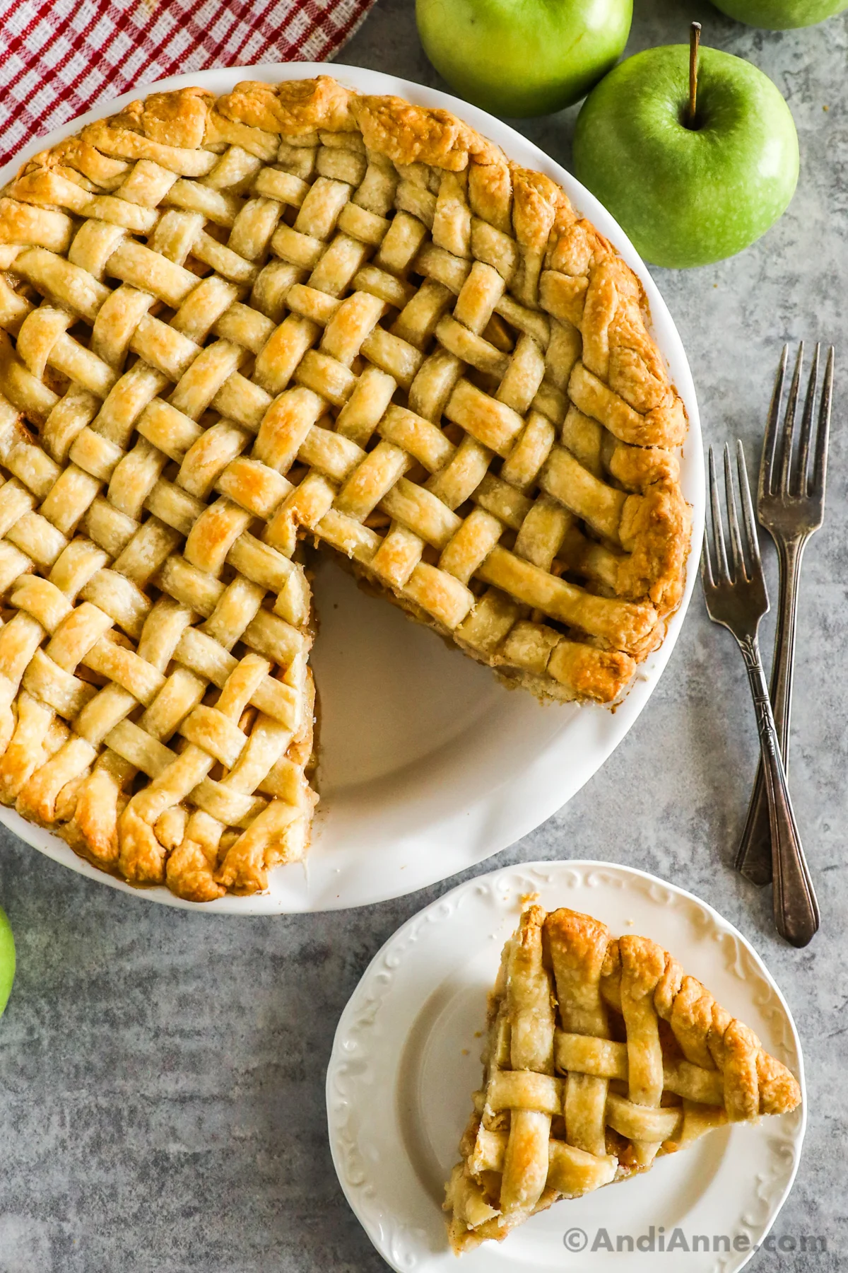 A slice cut out of lattice crust pie in white pie dish with two forks. Pie slice on plate.