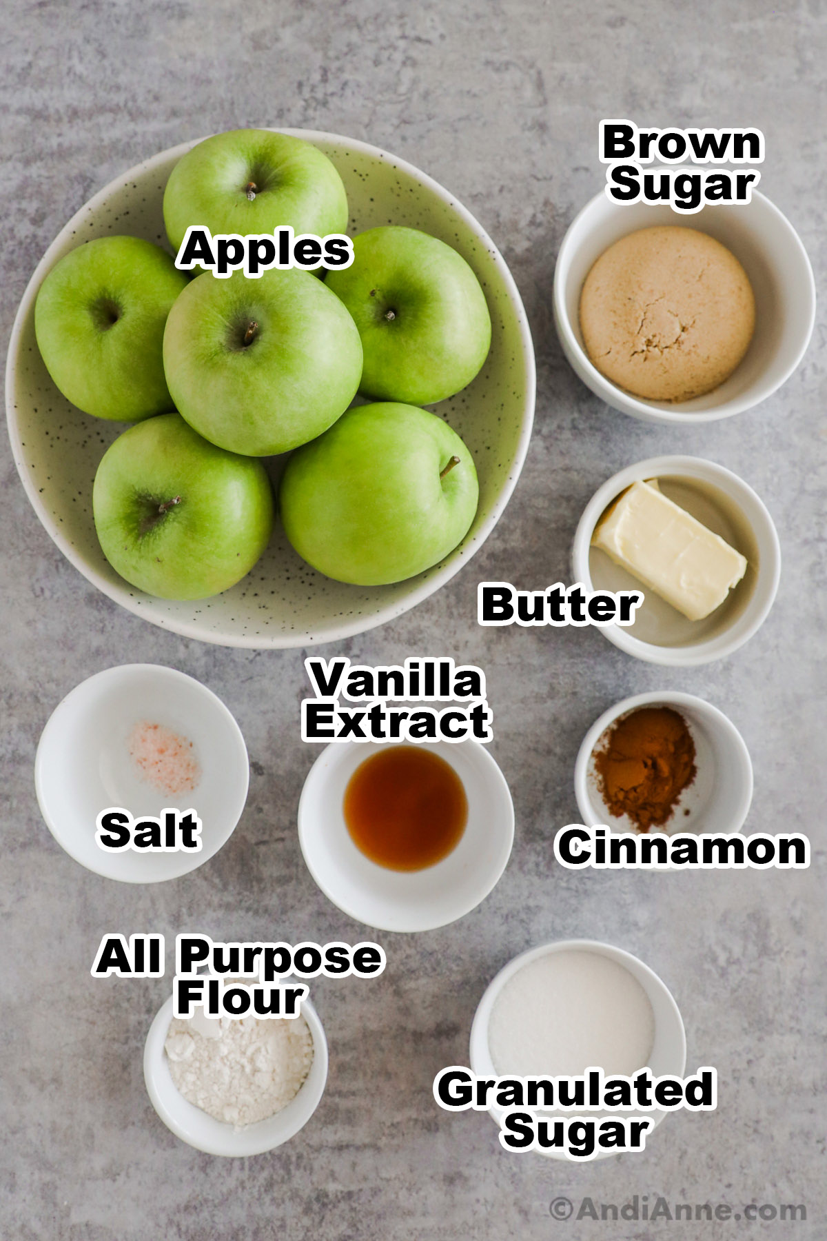 Recipe ingredients including bowl of granny smith apples, bowls of brown sugar, butter, flour, cinnamon, vanilla extract, salt, and granulated sugar.