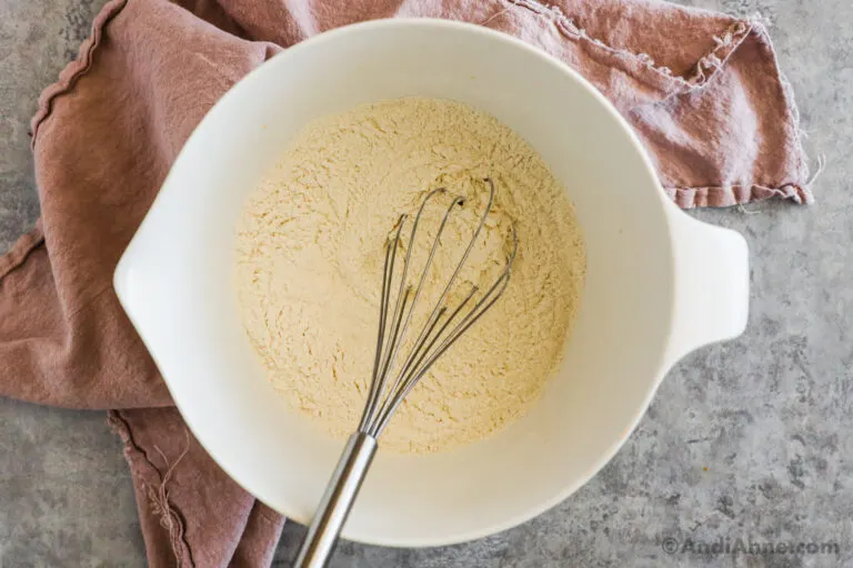 White bowl with dry ingredients and a whisk.
