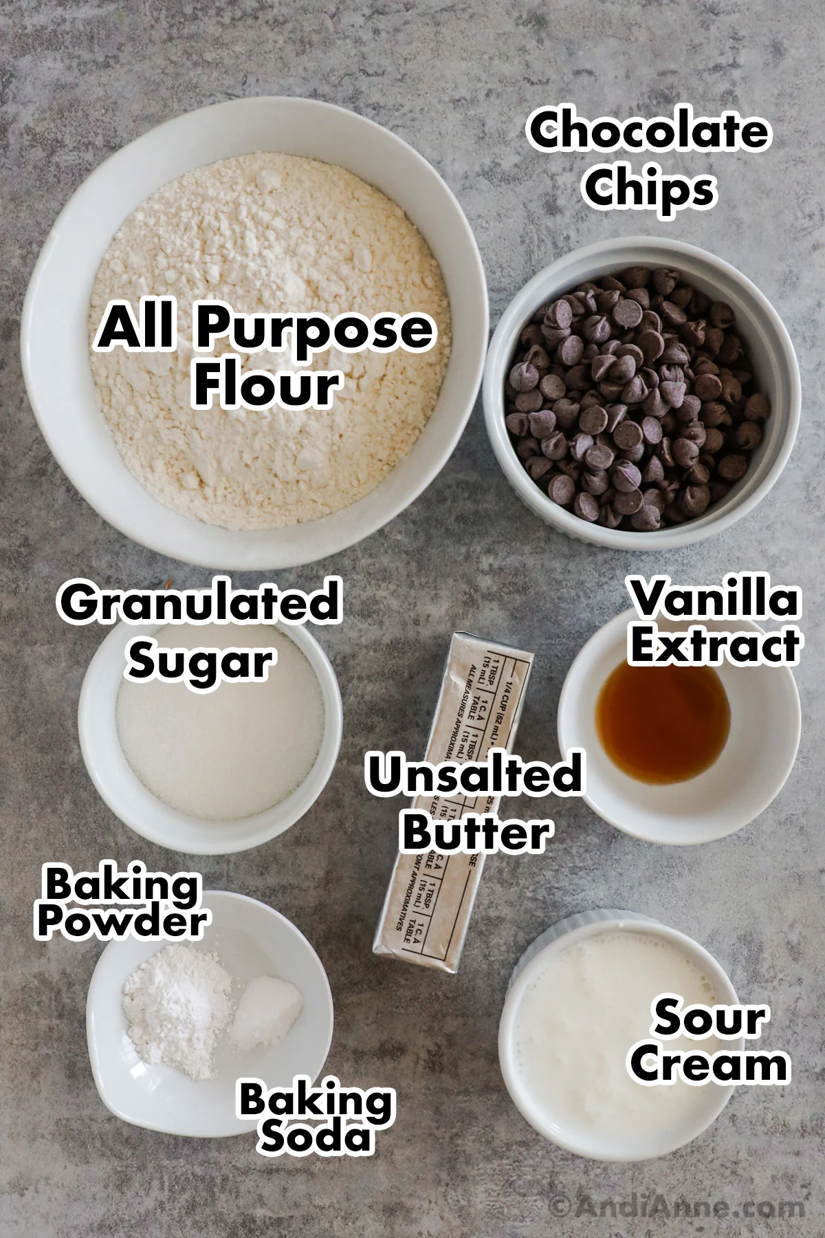 Recipe ingredients on the counter including bowls of flour, chocolate chips, sugar, vanilla extract, baking powder, sour cream and a stick of butter.