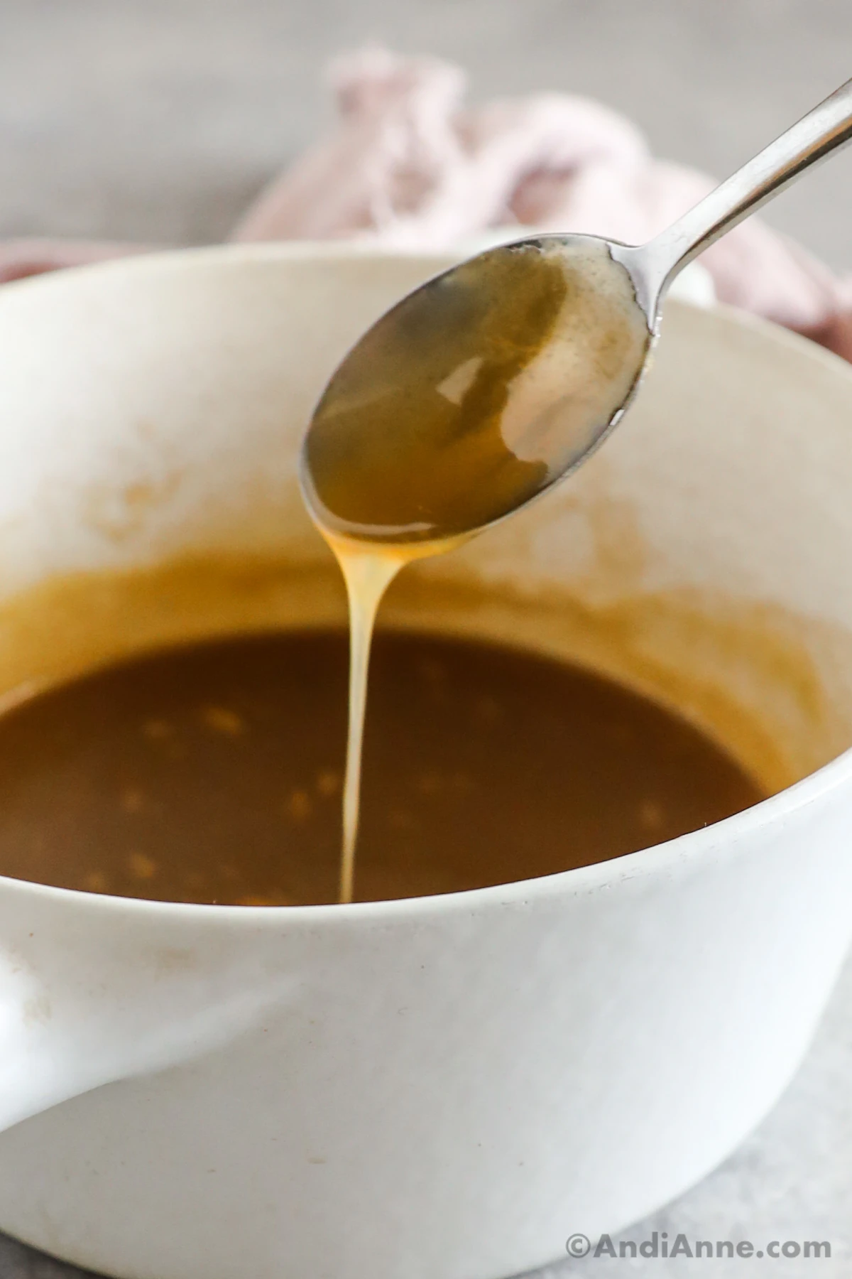 A spoon drizzling caramel sauce overtop of a saucepan.