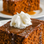 Two slices of gingerbread cake topped with caramel sauce and whipped cream.