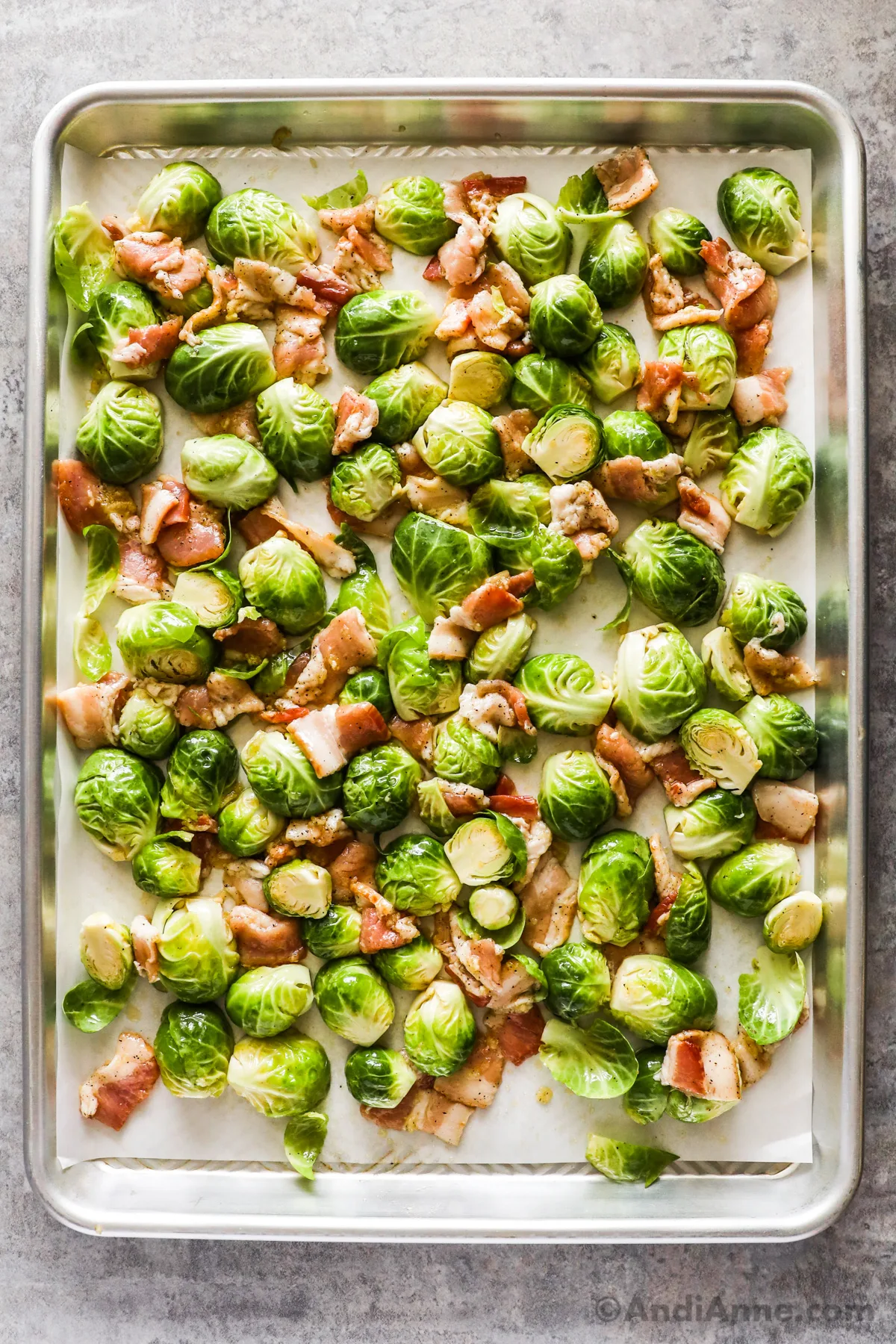 Raw sliced brussels sprouts and bacon pieces on a baking sheet.