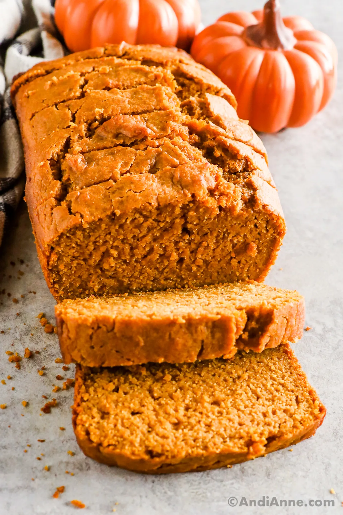 Sliced pumpkin bread loaf with pumpkins in the background.