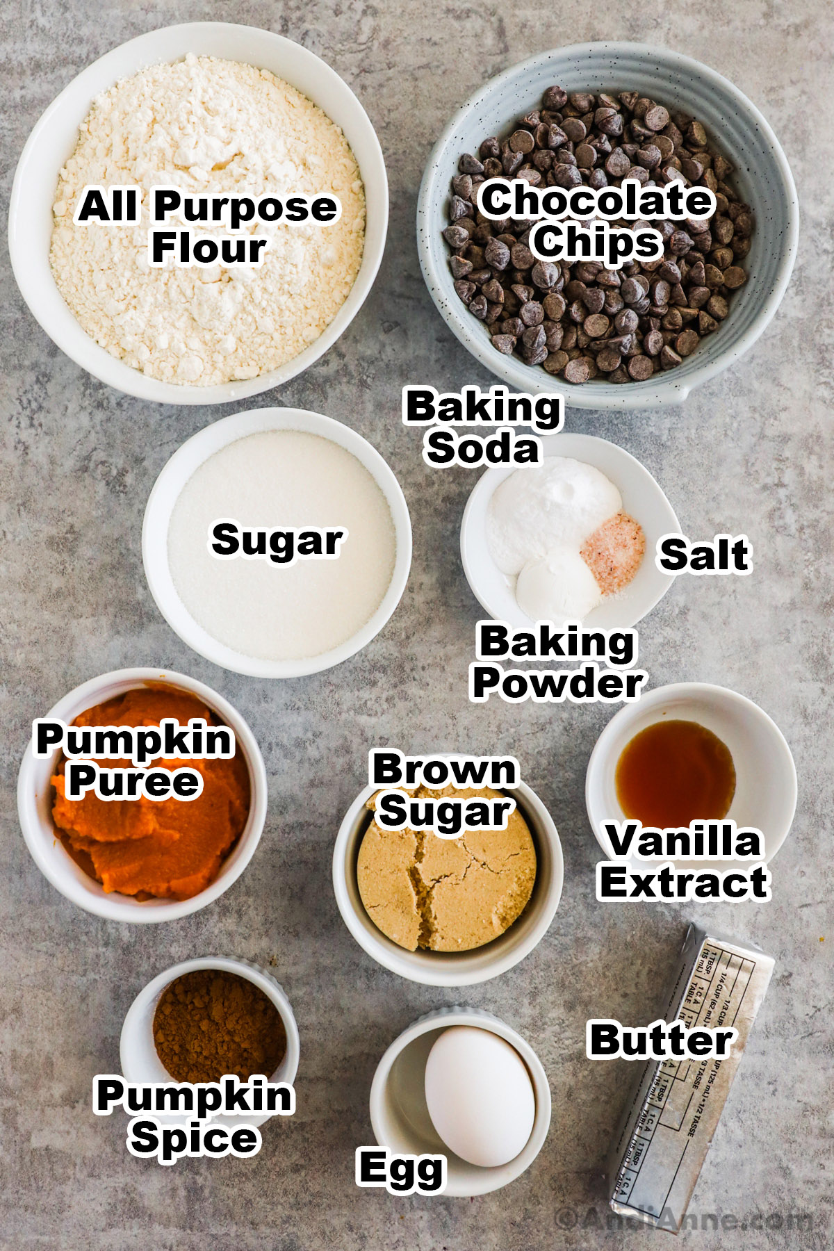 Bowls of recipe ingredients including flour, chocolate chips, white sugar, brown sugar, vanilla extract, pumpkin puree, pumpkin pie spice, egg and butter.