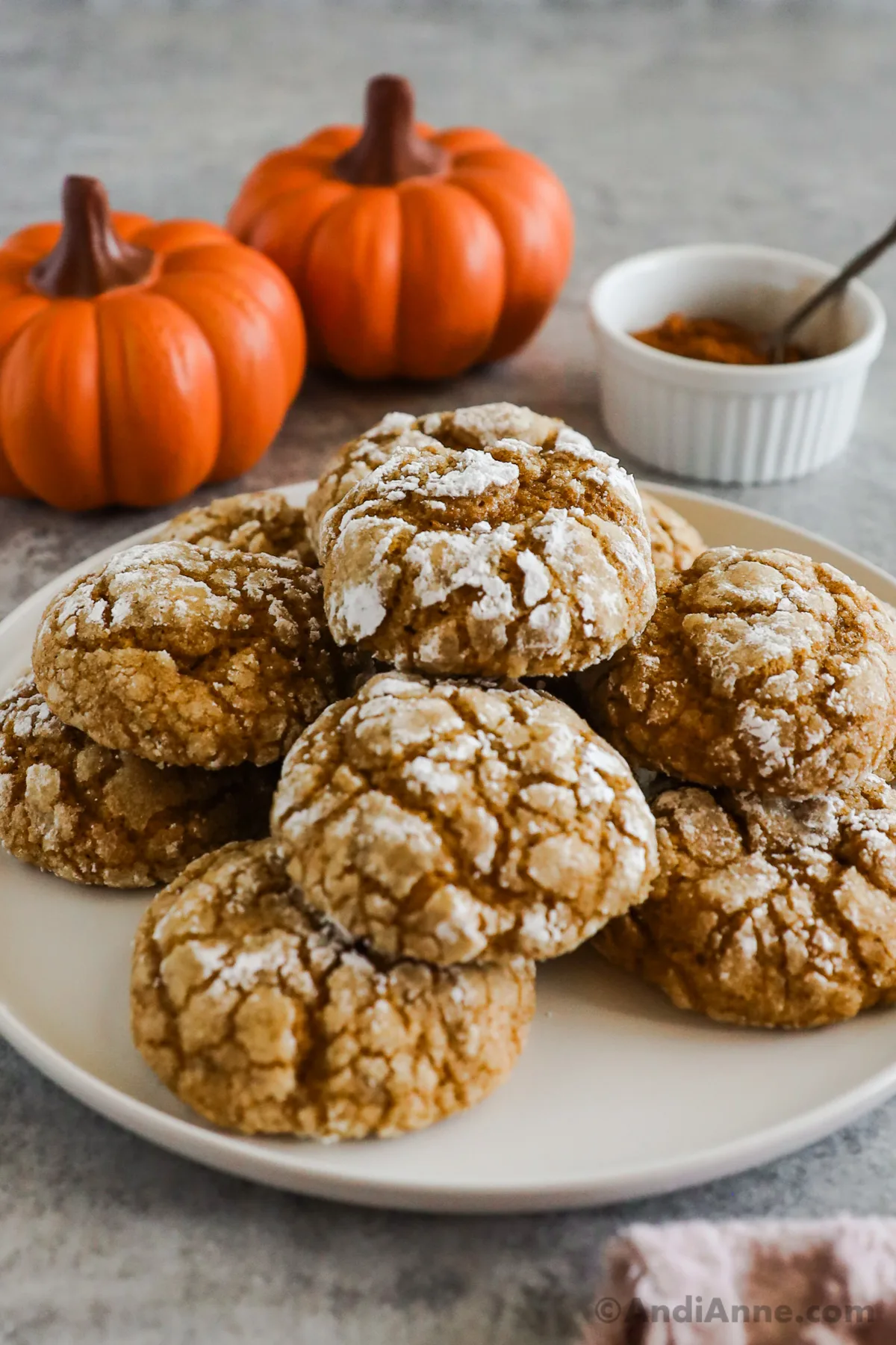 A pile of pumpkin crinkle cookies on a plate with pumpkin ornaments in background.