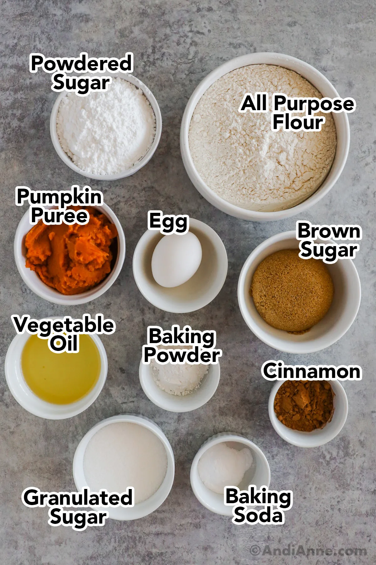 Recipe ingredients on the counter in bowls including flour, sugar, pumpkin puree, brown sugar, egg, baking powder, vegetable oil, cinnamon, sugar and baking soda.
