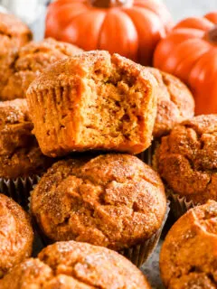 A pile of pumpkin muffins, one with a bite taken out of it.