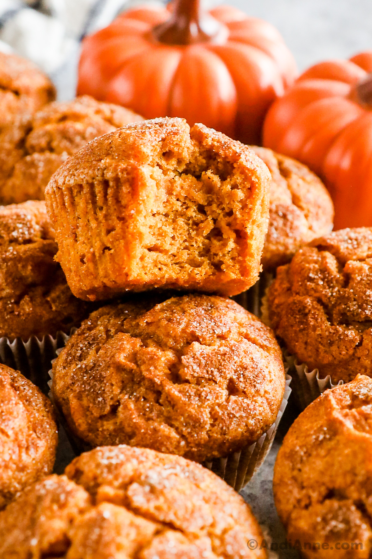 Close up of a pile of pumpkin muffins, one with a bite taken out of it.