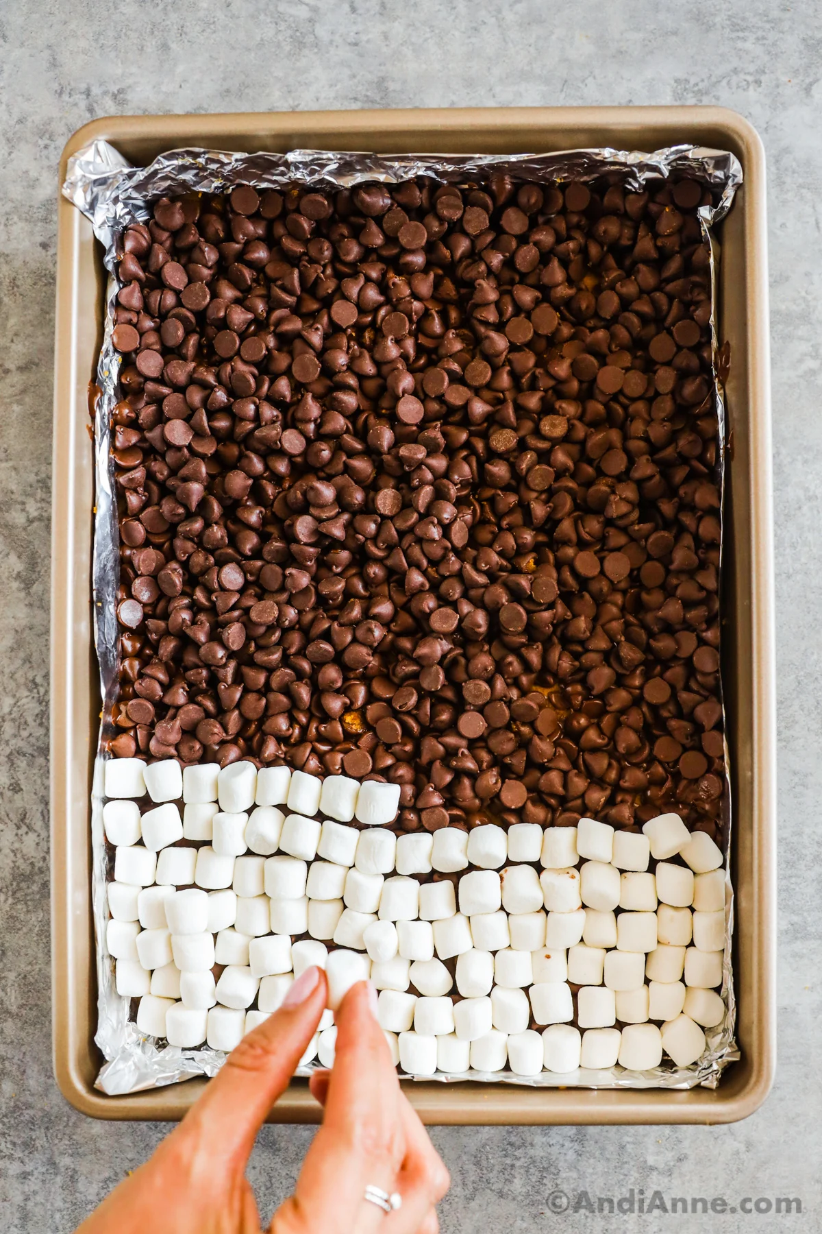 Overhead view of the process involving placing the mini marshmallows on top of the chocolate chip layer.