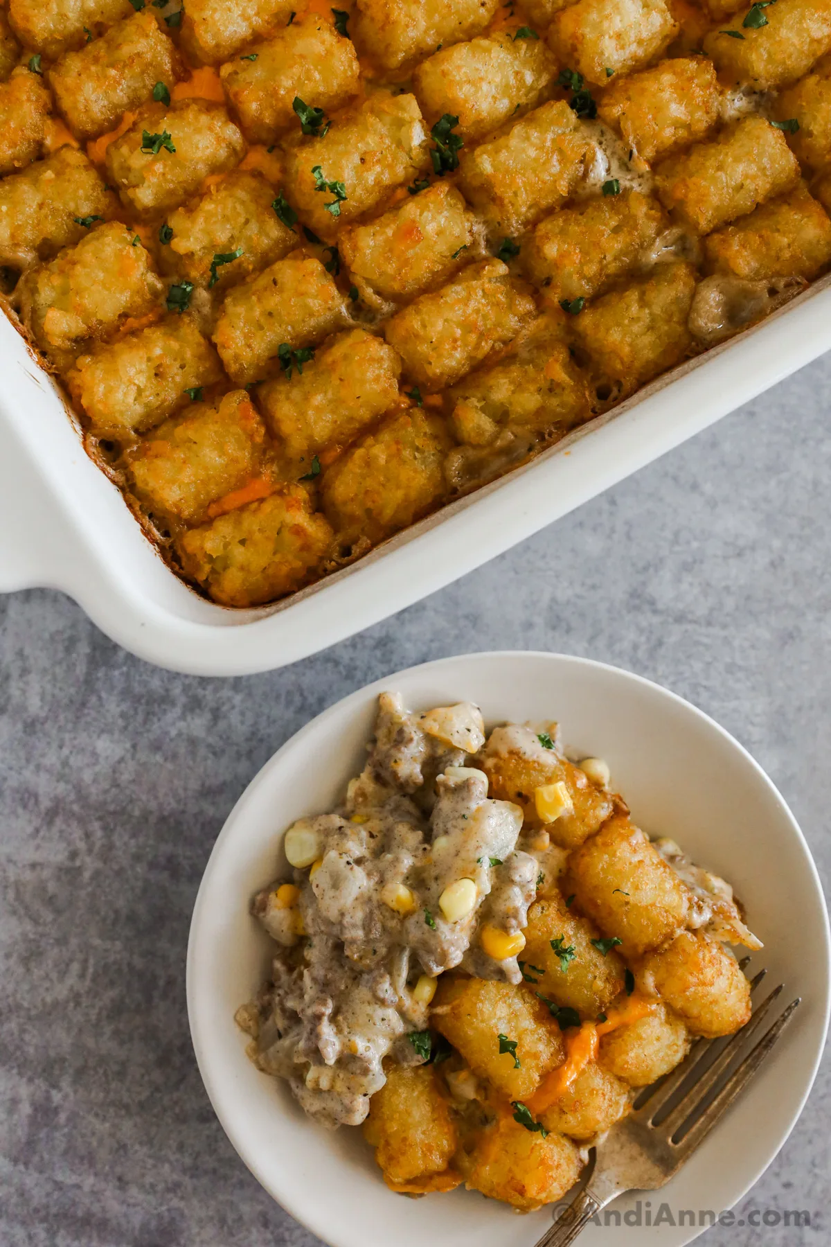 overhead view of baked tater tot casserole in baking dish, next to it a bowl with a serving of the recipe. 