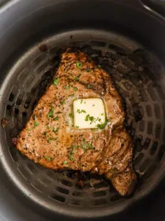 An air fryer steak topped with butter, in an air fryer.