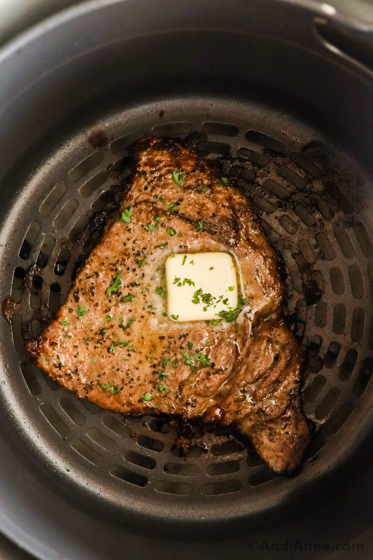 An air fryer with a cooked steak topped with butter