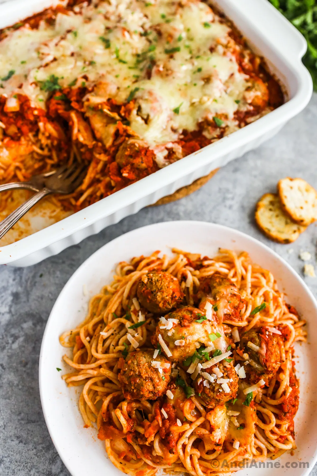 A plate of spaghetti and meatballs and a casserole dish with recipe in background.