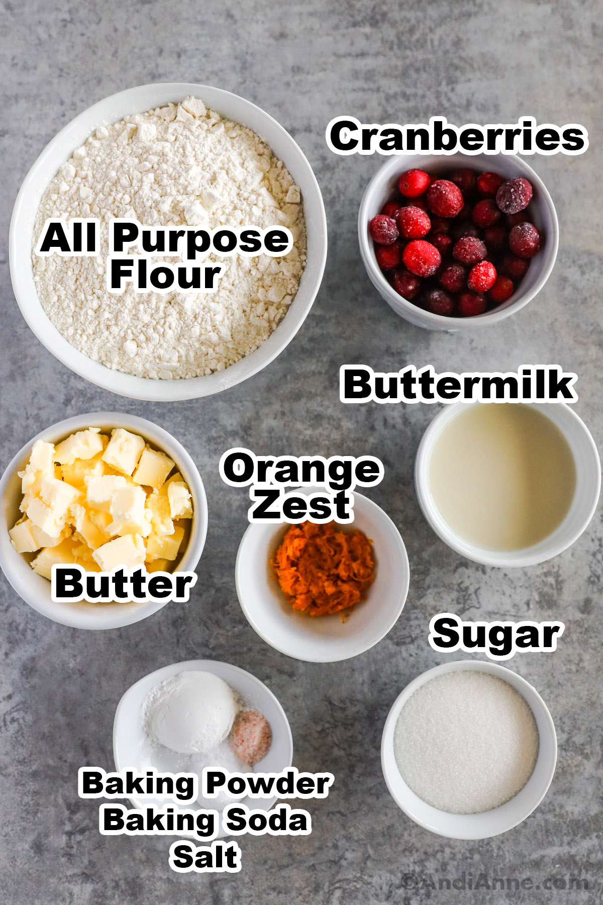 Recipe ingredients including bowls of flour, frozen cranberries, buttermilk, orange zest, cubed butter, sugar and baking powder.