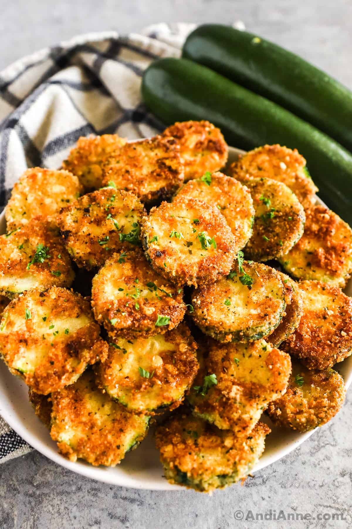 Crispy pan fried zucchini on a plate with fresh zucchini in background.