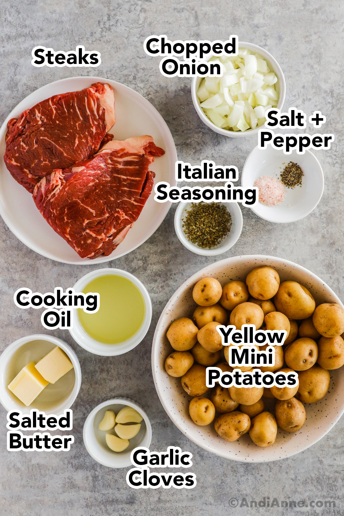 Recipe ingredients in bowls including two raw steaks, mini potatoes, onion, italian seasoning, salt and pepper, cooking oil, butter and garlic.