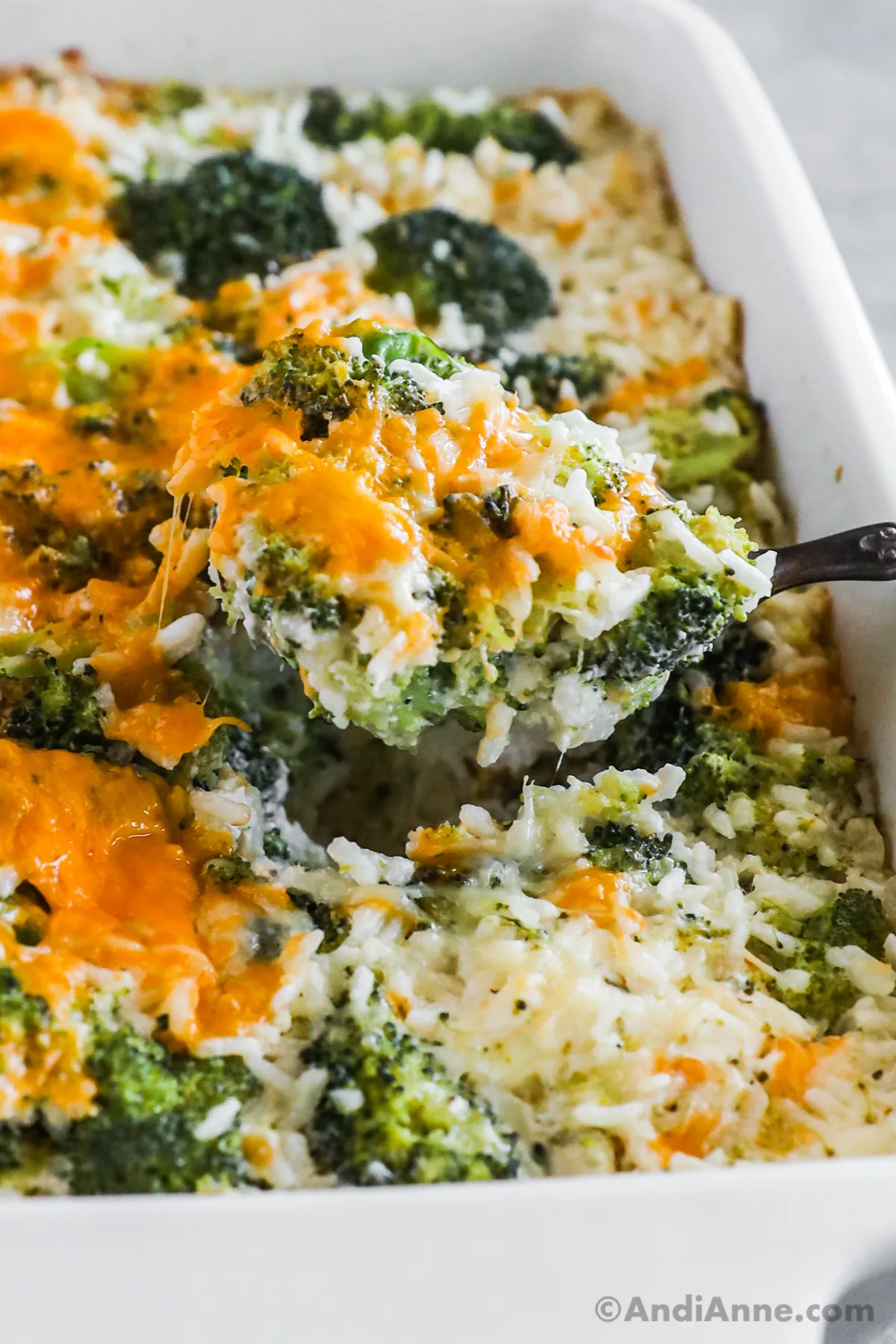 Close up of a spoon scooping some broccoli cheese rice casserole from the dish.