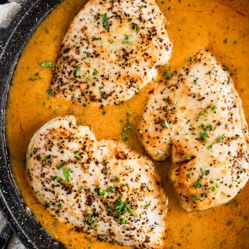 Cooked chicken breasts in gravy in a pan.