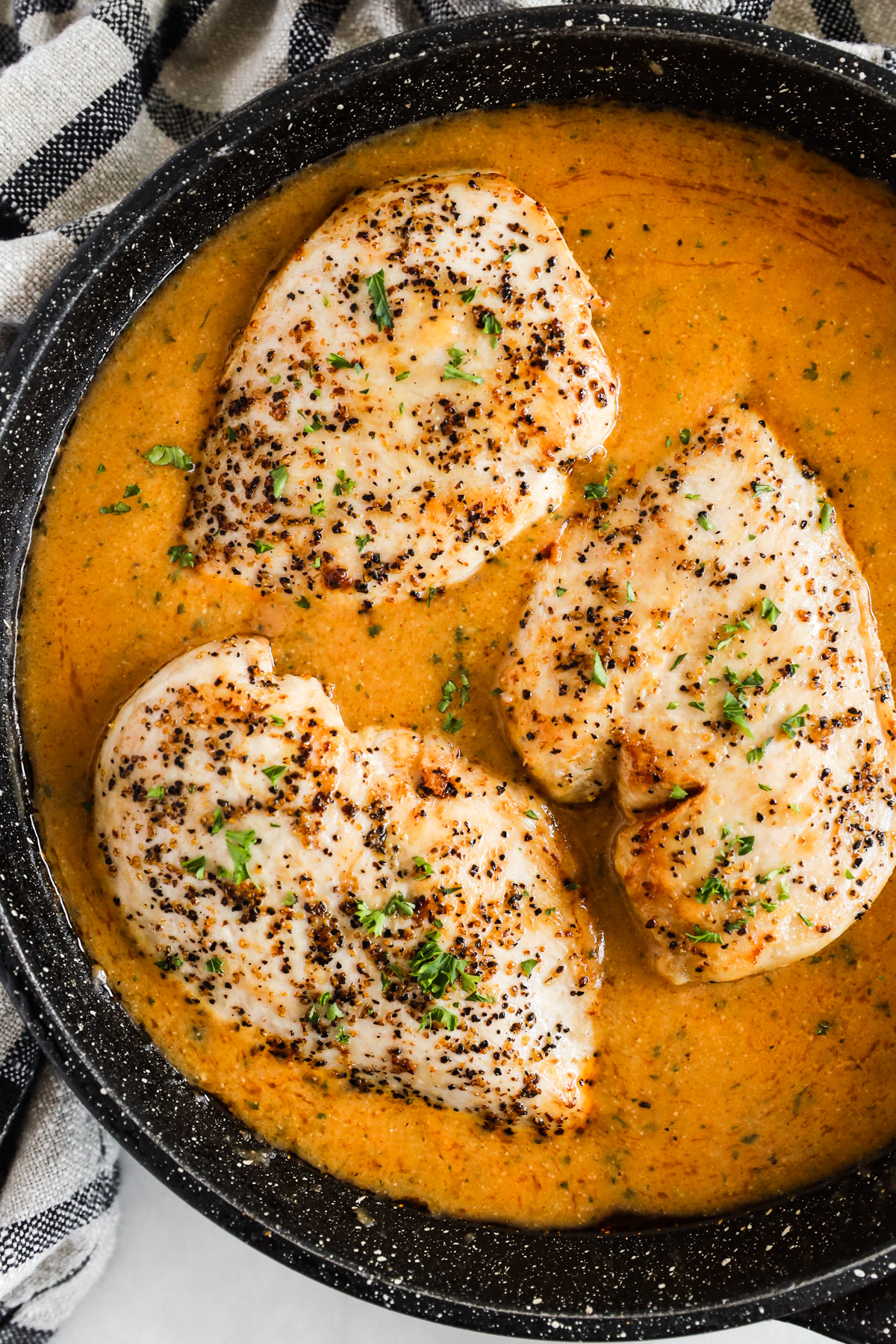 Cooked chicken breasts in gravy in a pan.