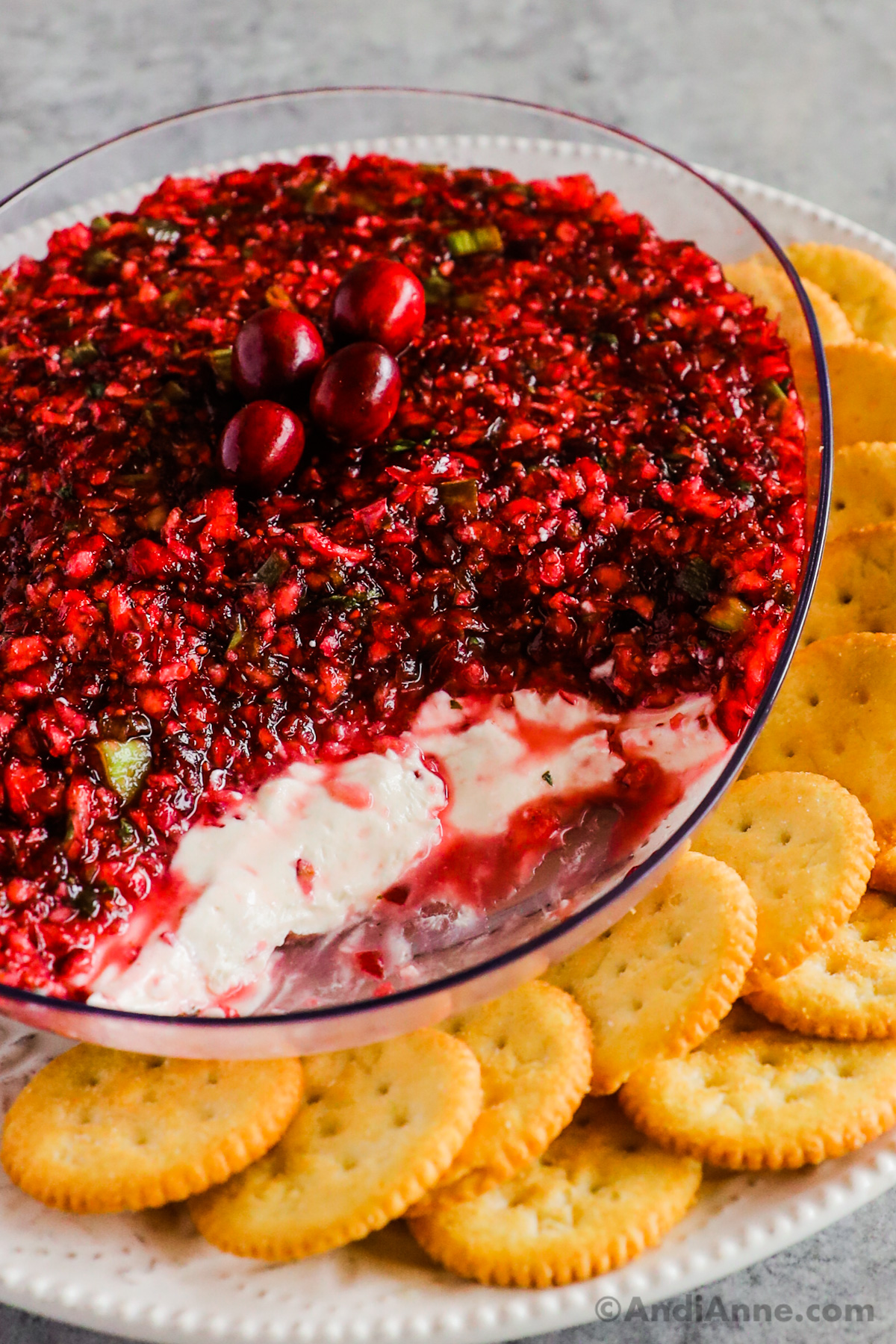 Close up of a bowl of cranberry jalapeno dip with a cream cheese layer and crackers on the side.