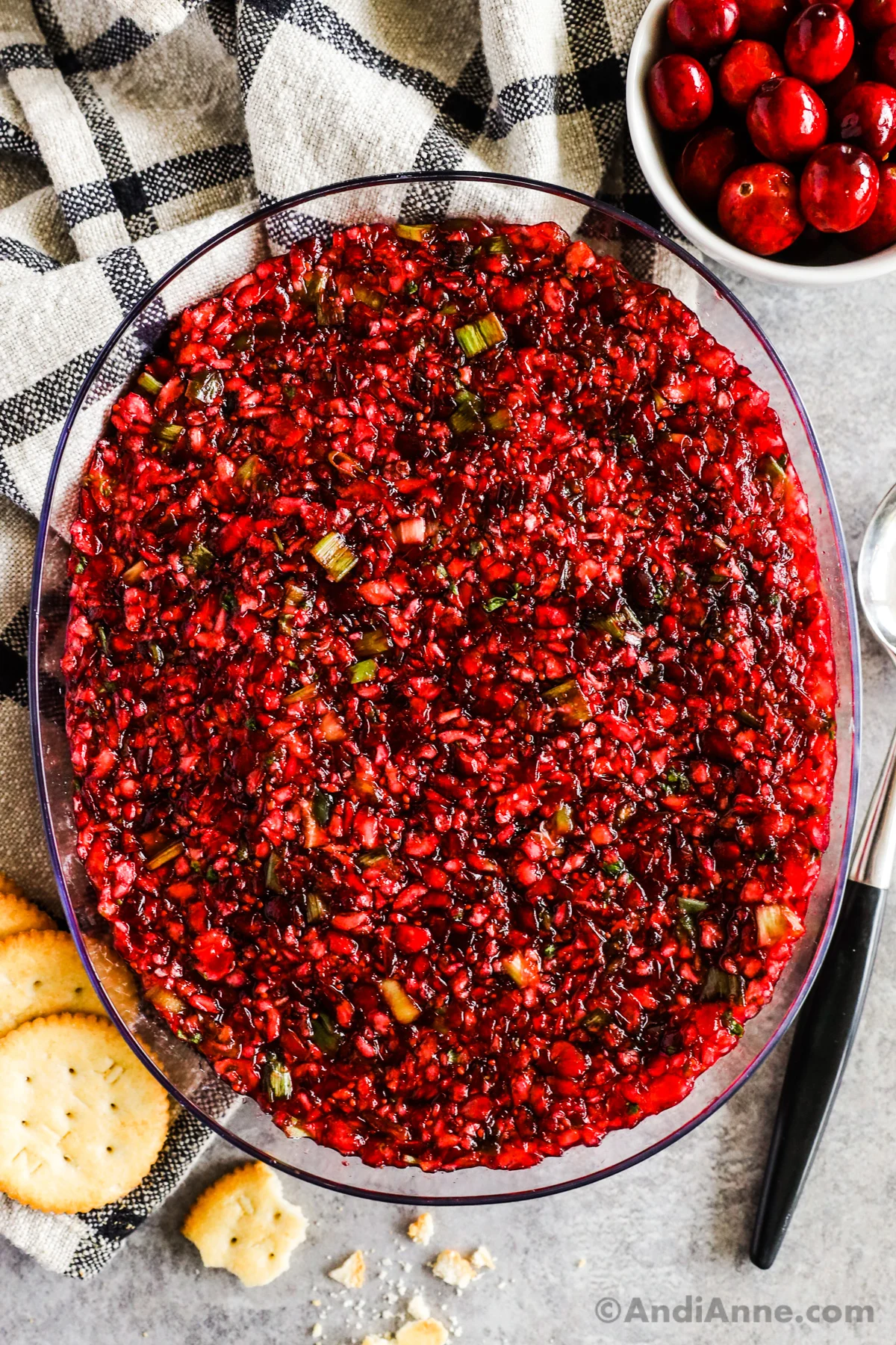 Cranberry jalapeno dip in a bowl with a few crackers, fresh cranberries and a spoon beside it.