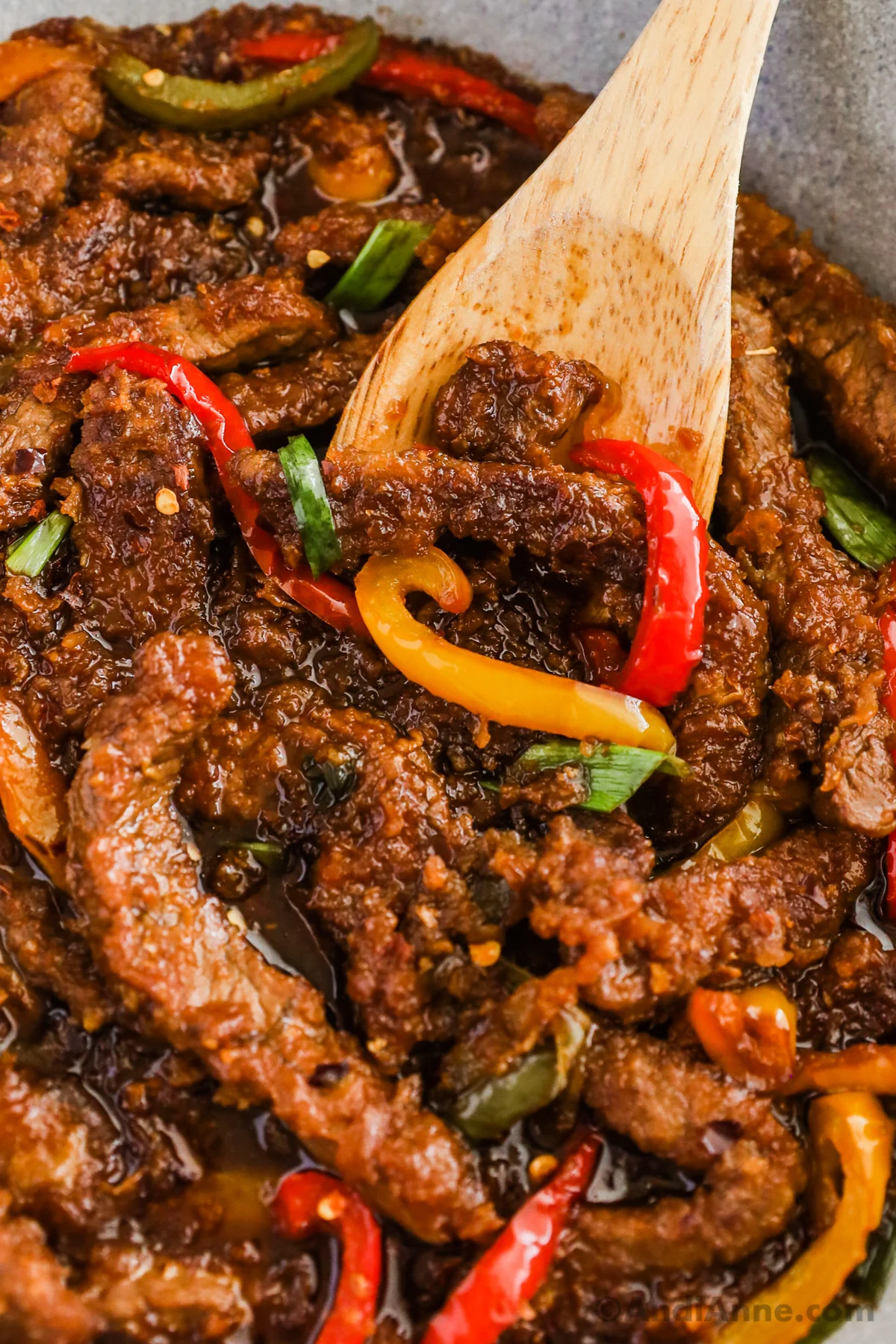 mongolian beef with beel pepper in a pan with a wood spoon