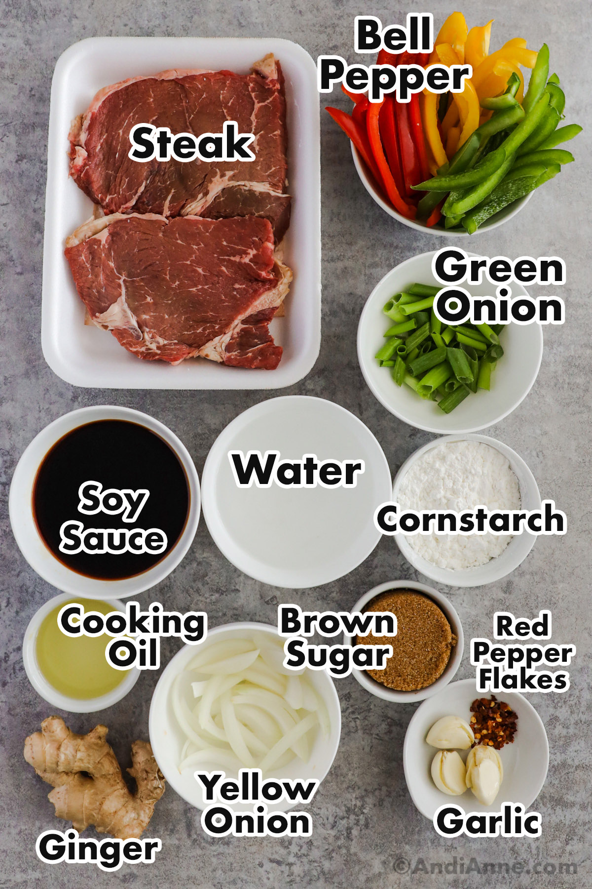 Recipe ingredients on the counter including raw steaks, sticks of bell pepper, chopped green onion, bowls of soy sauce, cornstarch, cooking oil, brown sugar, ginger, garlic and red pepper.