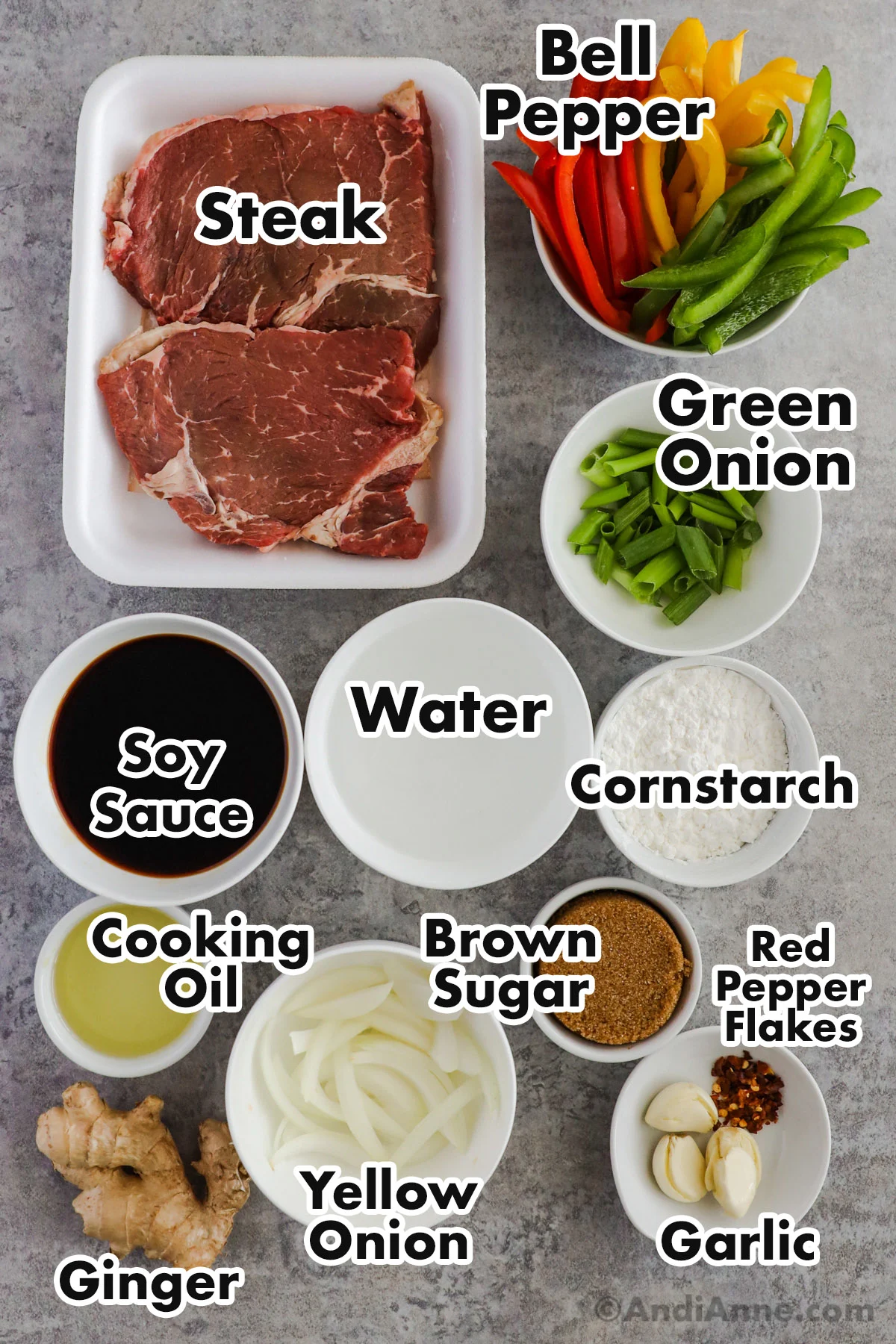 Recipe ingredients on the counter including raw steaks, sticks of bell pepper, chopped green onion, bowls of soy sauce, cornstarch, cooking oil, brown sugar, ginger, garlic and red pepper.
