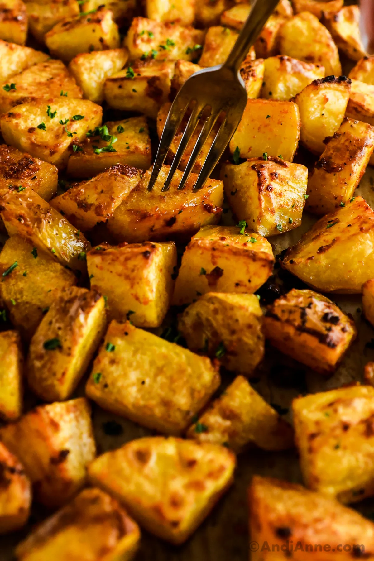 A fork piercing a crispy potato on a baking sheet.